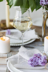 Beautiful table decor for a wedding dinner with a spring blooming lilac flowers. Celebration of a special event. Fancy white plates, wineglasses, candles. Countryside style