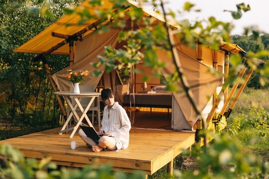 weekend work, Woman starts her morning working on a laptop while sitting near a tent in a glamping site for tourists