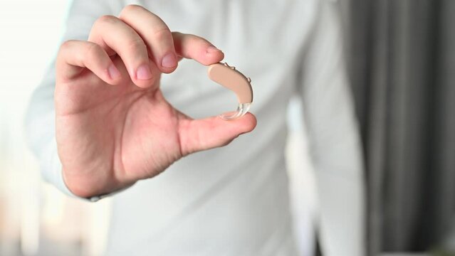 Close up of man  holding hearing aid equipment. The hearing aid lies in the man palm. Hearing aid concept. Man holding hearing aid equipment.