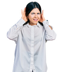 Young brunette woman with blue eyes wearing oversize white shirt trying to hear both hands on ear gesture, curious for gossip. hearing problem, deaf