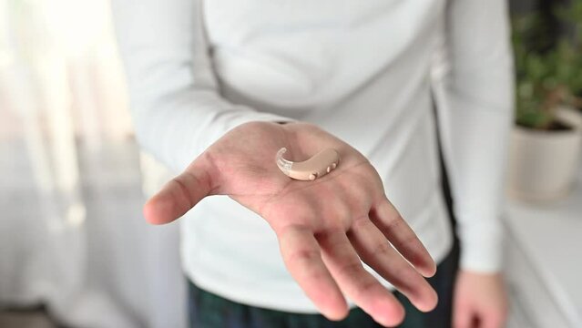 Close up of man  holding hearing aid equipment. The hearing aid lies in the man palm. Hearing aid concept. Man holding hearing aid equipment.