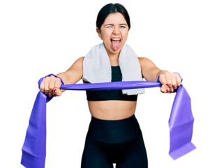 Young brunette woman with blue eyes training arm resistance with elastic arm bands sticking tongue out happy with funny expression.