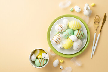 Easter concept. Top view photo of green plate and bowl with colorful easter eggs knife fork ceramic bunny and white feathers on isolated beige background