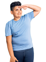 Little boy kid wearing sports workout clothes very happy and smiling looking far away with hand over head. searching concept.