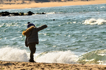 Little boy throwing stone into the sea on the beach in winter