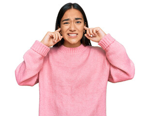 Young asian woman wearing casual winter sweater covering ears with fingers with annoyed expression...