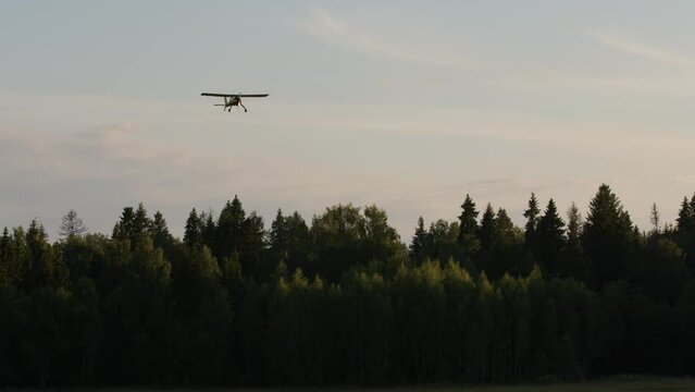 small bright yellow-red civilian small plane slows down and lands in the airfield. a propeller plane on a runway with trees in the background is landing. Sun shine in camera.