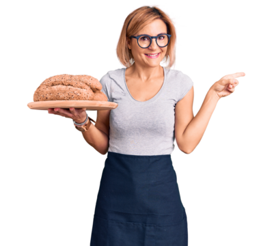 Young blonde woman holding wholemeal bread smiling happy pointing with hand and finger to the side