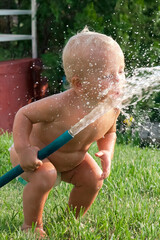 Child toddler boy playing with water hose outdoors in summer, summer activities 