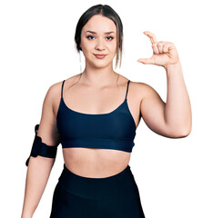 Young hispanic woman wearing sportswear smiling and confident gesturing with hand doing small size sign with fingers looking and the camera. measure concept.