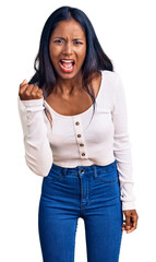 Young indian girl wearing casual clothes angry and mad raising fist frustrated and furious while shouting with anger. rage and aggressive concept.