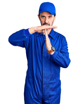 Middle age handsome man wearing mechanic uniform doing time out gesture with hands, frustrated and serious face