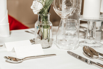Cutlery on a festive table in a restaurant, a name plate, a vase of flowers, a white candle, wine glasses and glasses for water and wine