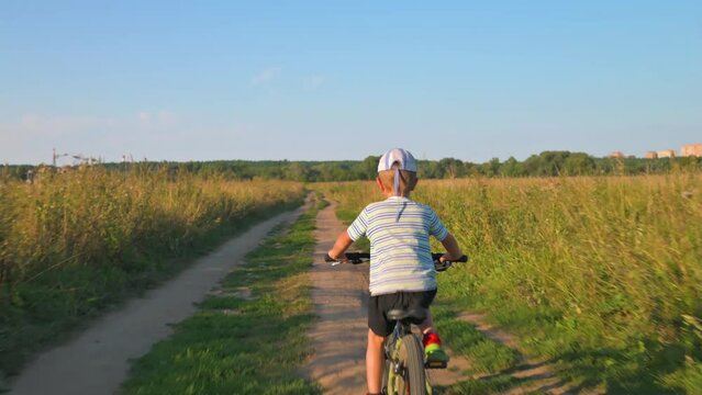 The boy riding his bike on a pathe along the field. 4k video footage 
