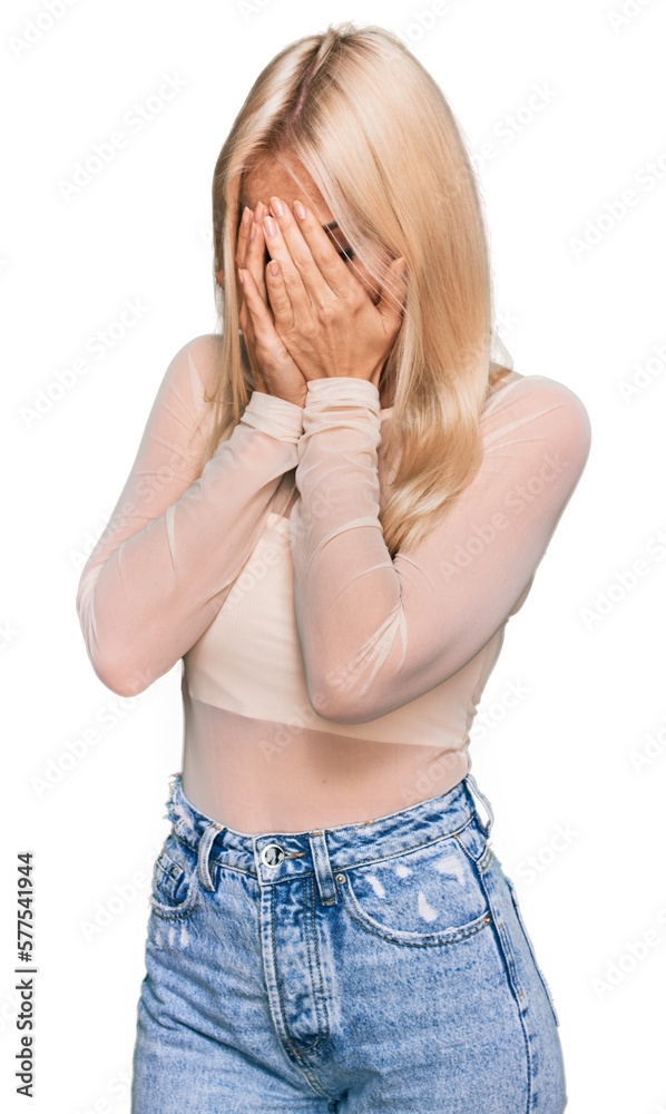 Sticker Young blonde woman wearing casual clothes with sad expression covering face with hands while crying. depression concept.