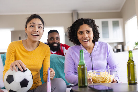 Happy diverse friends sitting on sofa, watching football match and supporting