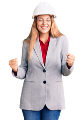 Beautiful young woman wearing architect hardhat very happy and excited doing winner gesture with arms raised, smiling and screaming for success. celebration concept.