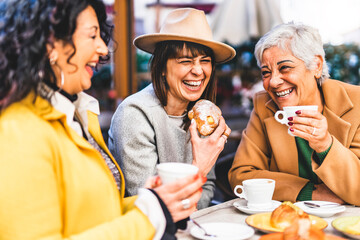 Group of senior women at bar cafeteria enjoying breakfast drinking coffee and eating croissant -...