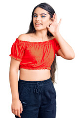 Fototapeta premium Brunette teenager girl wearing casual clothes smiling with hand over ear listening an hearing to rumor or gossip. deafness concept.
