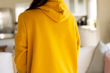 Midsection of biracial woman wearing yellow sweatshirt with copy space in living room - Powered by Adobe