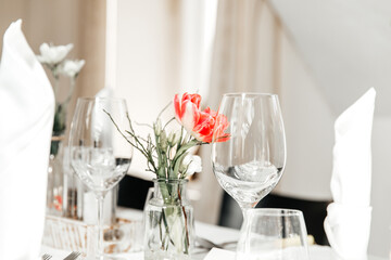 Festive decorated table in a restaurant, wine glasses, vase, flowers, mineral water bottles, textiles, cutlery on a white tablecloth. Restaurant, celebration