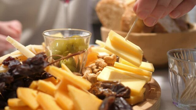 Delicious assorted cheeses on a wooden plate, a man's hand takes a piece for tasting.