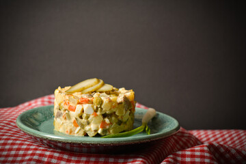 Side view of traditional rustic salad Olivier served in culinary rings Country Salad with potato, carrot, green peas, pickled cucumbers, eggs on American red checkered kitchen towel, black background