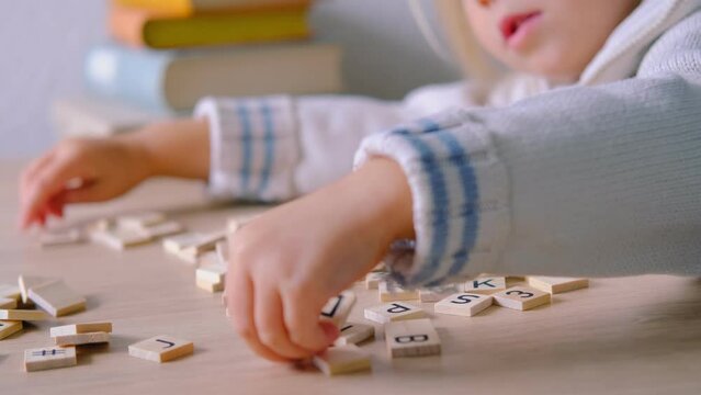 hands close-up, small child 3 years old plays wooden alphabet blocks, makes up words from letters, dyslexia awareness, learning difficulties, human brain development, happy childhood, selective focus