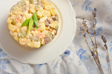 Top view of rustic salad Olivier served in culinary ring. Country Salad with potato, carrot, green peas, pickled cucumbers, eggs on cotton textile background with dried lavender flowers.