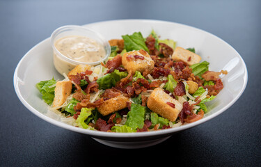 Traditional caesar salad in a white bowl on a black table. Selected focus. Healthy food style.