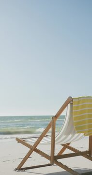 Vertical video of deck chair and towel on beach, in slow motion, with copy space