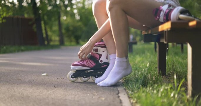 Woman sitting on park bench puts on rollerblades