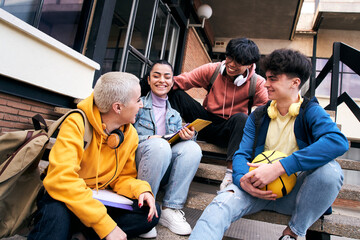 Group of happy young diverse colleagues talking and having fun together outdoors on college campus. Happy teenage students talking outside high school building. People in their leisure time.