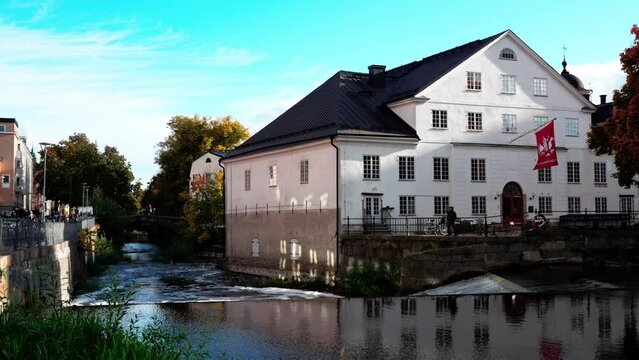 Uppsala, Sweden. View of the Fyrisån River and Upplandsmuseet, the Uppsala County Museum. Cultural and archaeological history of the city. People stroll along the river and on the bridge