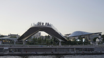 Obraz premium A walk along the river in the city center. Action. Tourist sites are right next to the river that flows next to the tall buildings,churches and shops of the city and walking people are visible.
