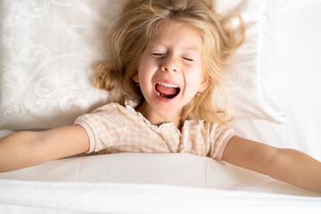 happy little girl in a white bed on a pillow, good morning, healthy baby sleep concept