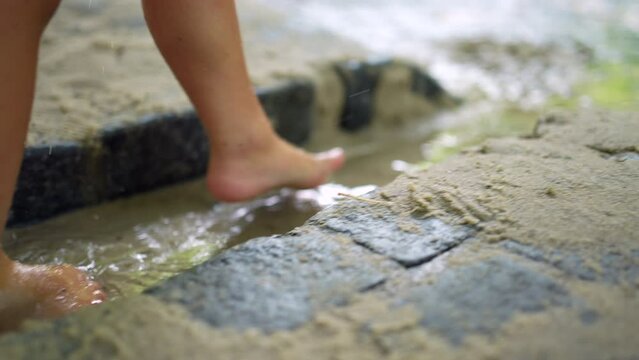 Little boy walking barefoot outside in water mud. Closeup child feet stepping in wet sand outdoors