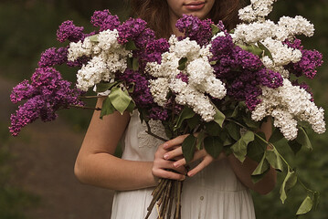 A young girl in the park hugs a large bouquet of lilacs. Girl in a white dress holding flowers