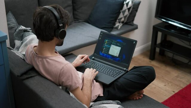 Caucasian man in headphones scrolling social media on laptop at home