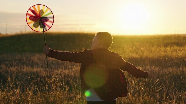Boy plays with turntable, autumn field. Happy boy playing with toy pinwheel outdoors in summer in park at sunset. Active Kid runs and holds colored wheel on stick in his hand. Family walk in autumn