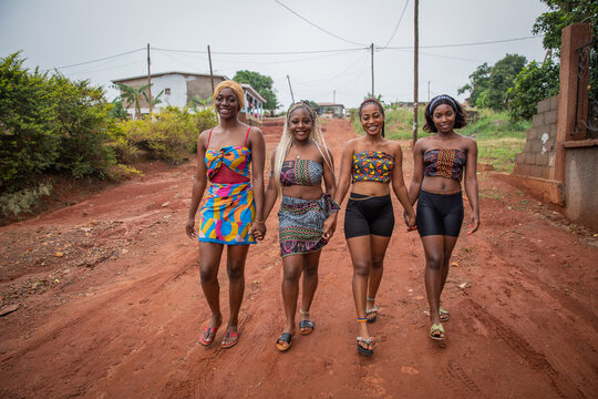 Four young smiling African women walk holding hands, women dressed with traditional African clothes