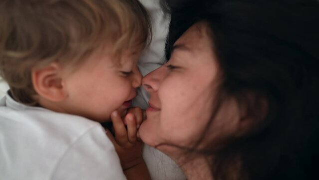 Mother and child love and care laying in bed. Lifestyle moment of mom and son eskimo kiss during weekend