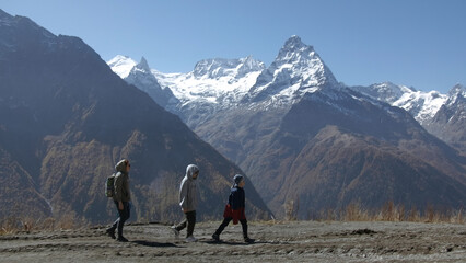 Family walks on background of mountain valley with snowy peaks. Creative. Women with child are walking in mountain valley on sunny day. Family hiking with child in valley with rocky mountains