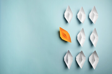 Yellow paper boat floating away from others on light background, flat lay with space for text. Uniqueness concept