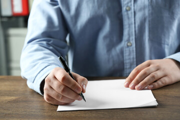 Man writing on sheet of paper with pen at wooden table, closeup