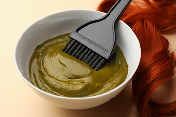 Bowl of henna cream, brush and red strand on beige background, closeup. Natural hair coloring