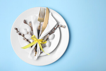 Festive table setting with willow twigs on light blue background, top view with space for text. Easter celebration