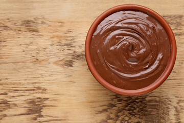 Bowl of chocolate paste on wooden table, top view. Space for text