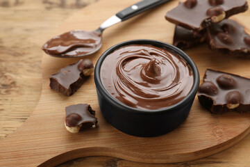 Chocolate pieces and bowl of sweet paste on wooden table, closeup
