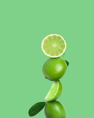 Stacked whole and cut limes on light green background